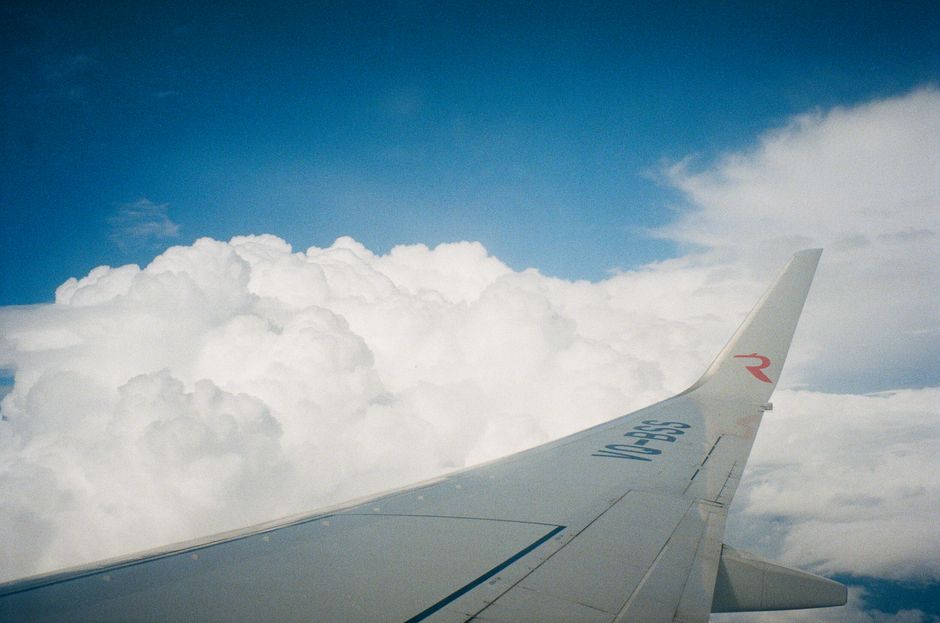 View of an airplane wing flying above fluffy white clouds under a clear blue sky.