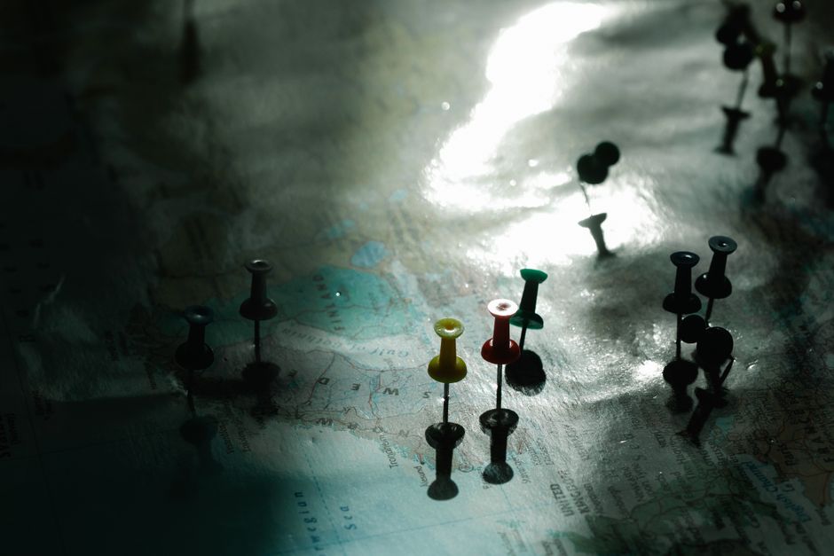 A map with colored pins under dramatic light, highlighting travel planning and destinations.